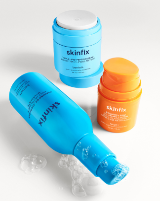 Assortment of Skinfix products including Triple Lipid-Peptide Cream, Brighten + Firm 15% Vitamin C Serum and Foaming Oil Cleanser on beige background.
