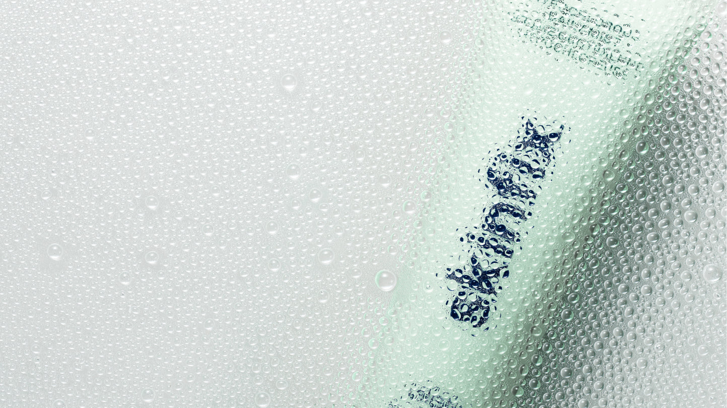 A close-up of a cosmetic tube with water droplets on its surface, showing dark blue text that reads 'SKINFIX'.