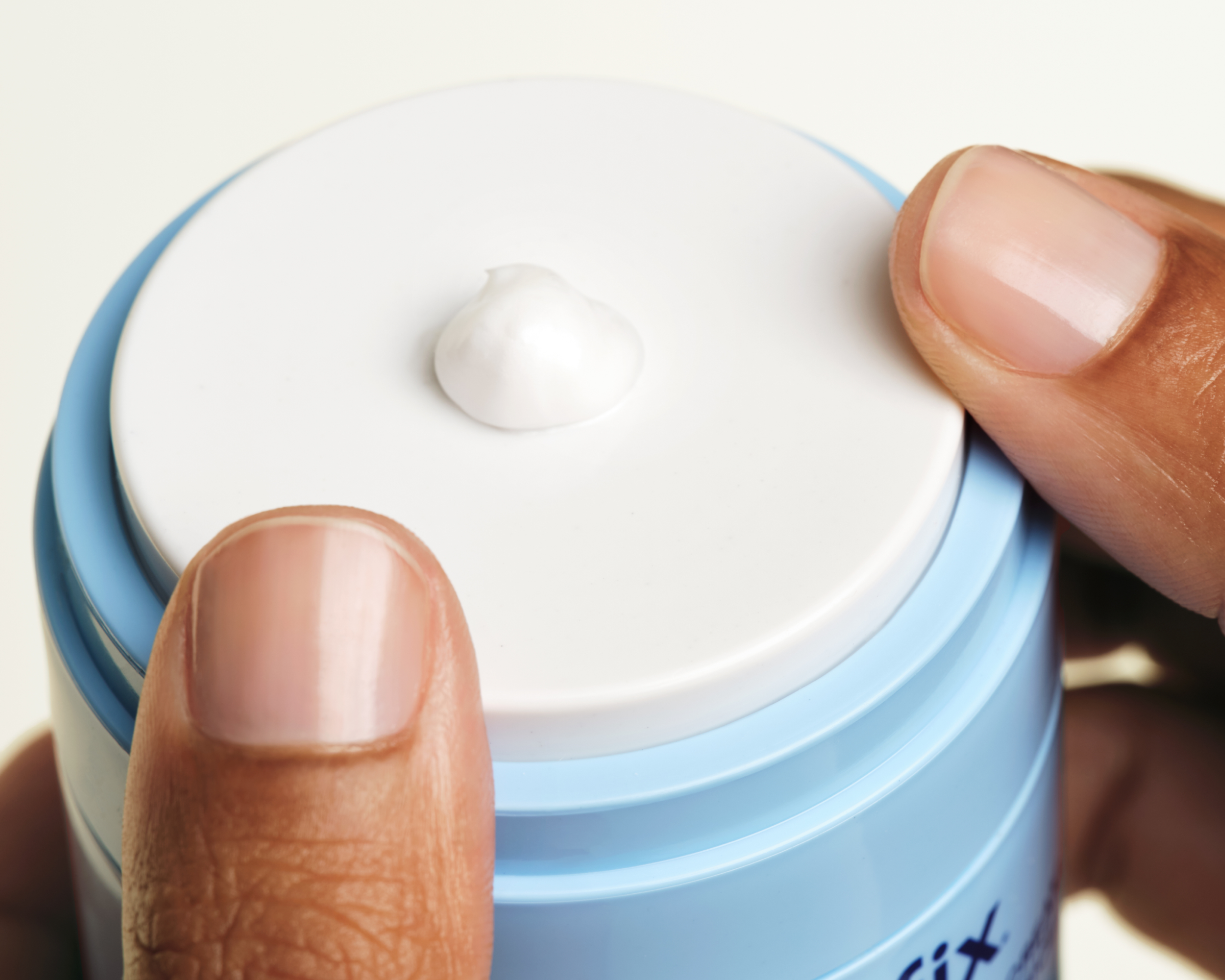 Hands pumping the Skinfix Ceramide Prime Whipped Cream jar, with a small dollop of white cream resting on the lid.