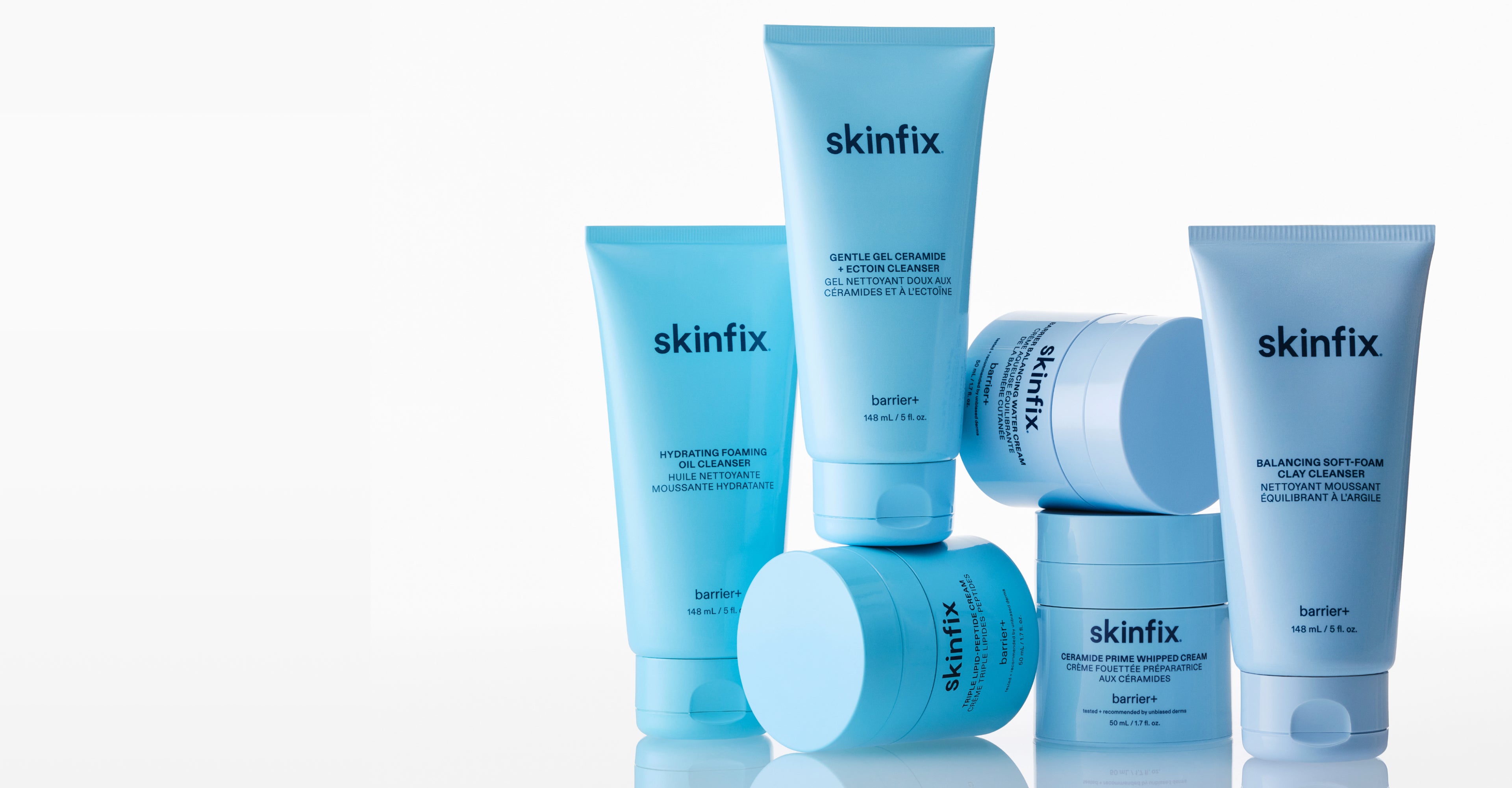 A group of Skinfix skincare products in light blue packaging, including tubes and jars, arranged on a reflective white surface against a white background.