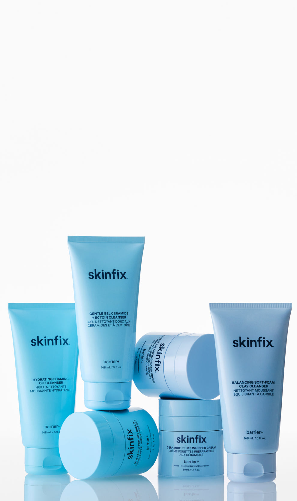A group of Skinfix skincare products in light blue packaging, including tubes and jars, arranged on a reflective white surface against a white background.