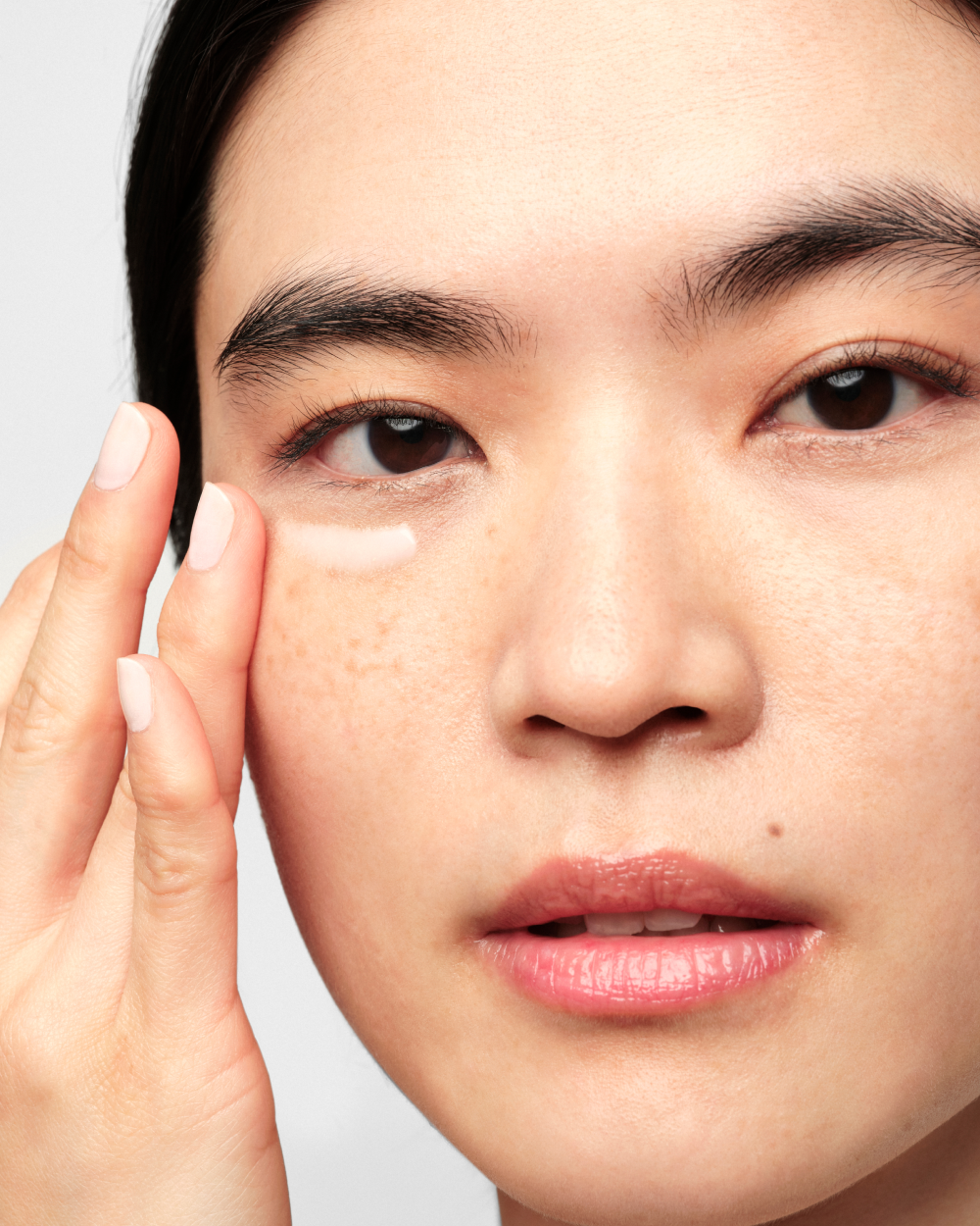 Woman looking into camera applying cream under her eye with fingertip.