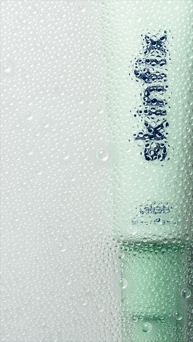 A close-up of a clear glass bottle covered in water droplets, with the brand name 'SKINFIX' visible through the condensation. The bottle has a pale mint green tint and is set against a white/gray background.