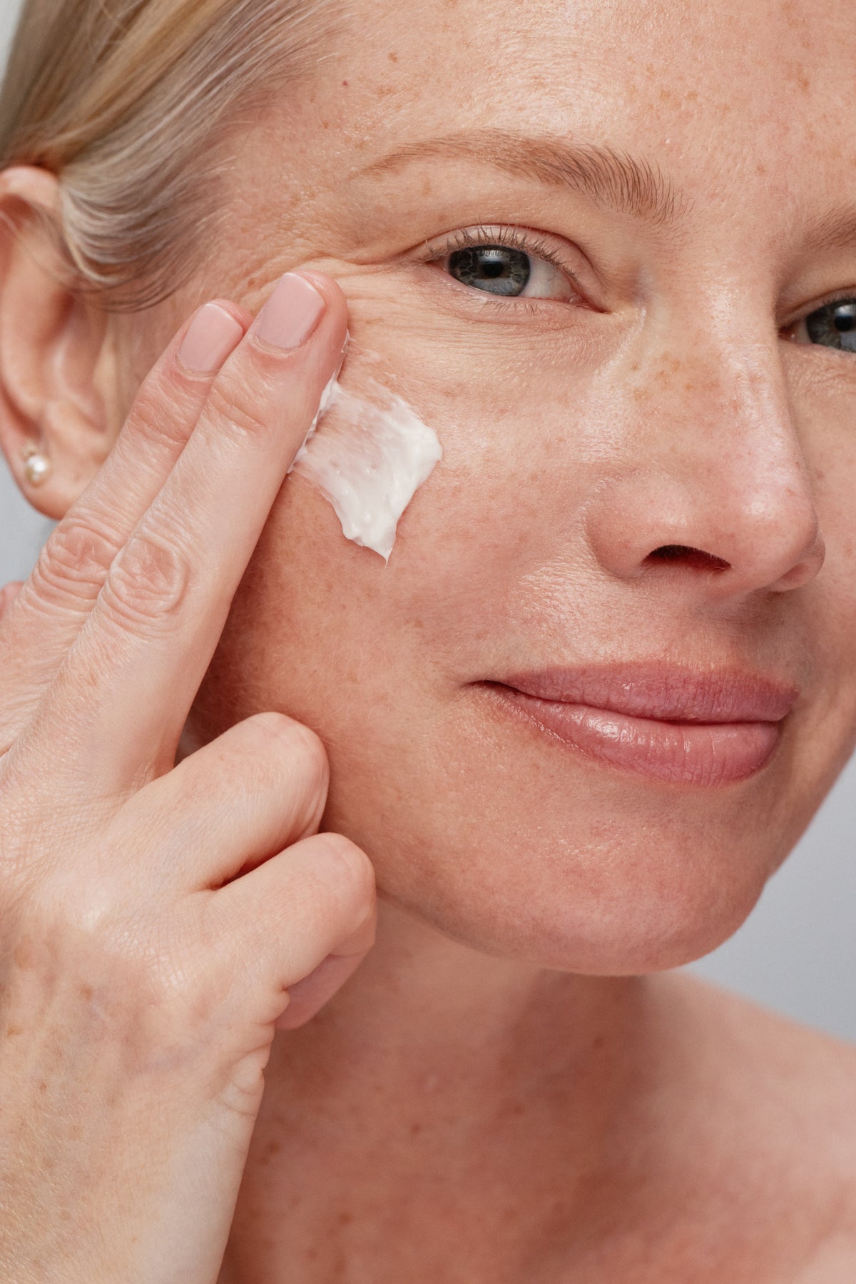 Woman applying cream to her face with a neutral background